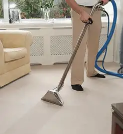 Professional carpet cleaner using a hot-water extraction wand and hose machine in a living room in Atlanta, GA.