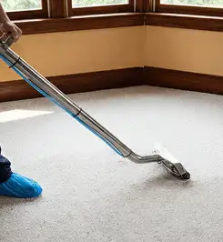 Steam carpet cleaning technician using a hot-water extraction wand on a residential carpet, wearing blue protective shoe covers Atlanta, GA.