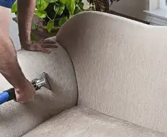 Professional upholstery cleaner deep-cleaning a fabric sofa with a handheld extraction tool and hose in Atlanta, GA.